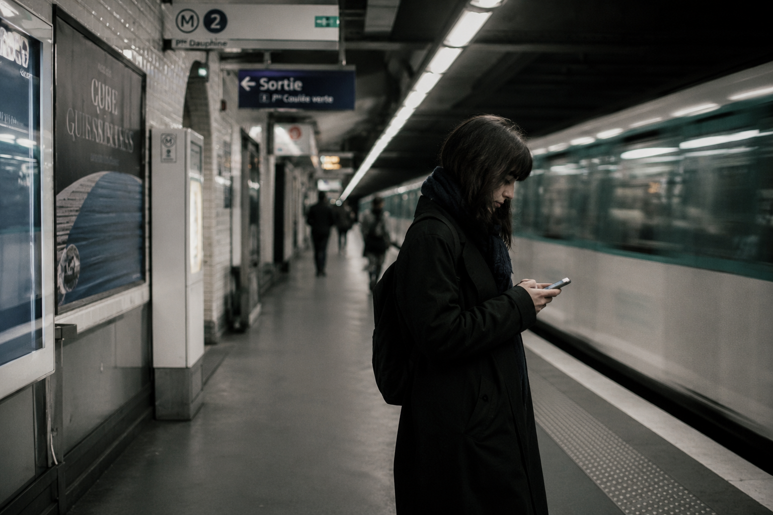 Femme consultant son téléphone sur un quai de métro, rame en mouvement en arrière-plan